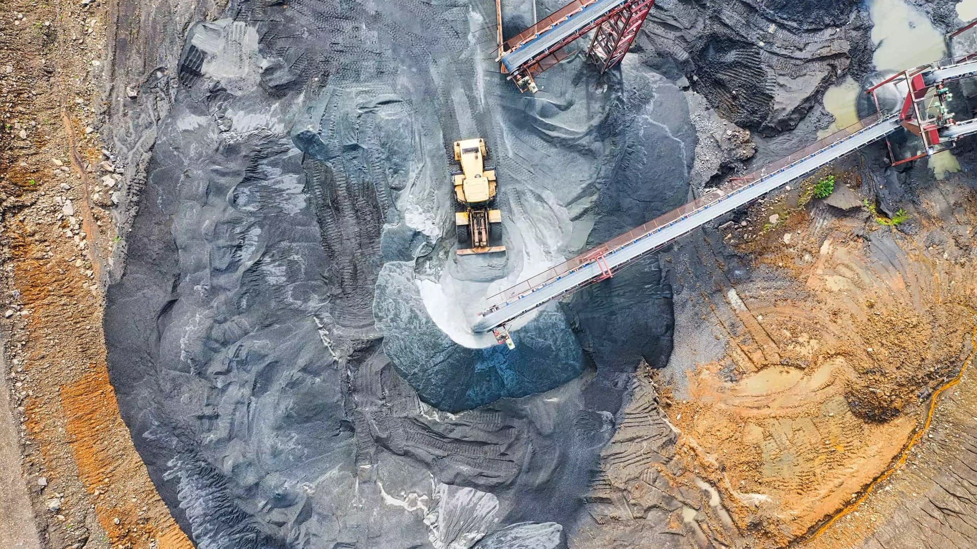 Aerial view of an open-pit mine with a loader and conveyor system